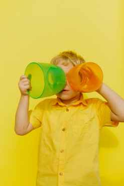 boy in yellow button up shirt holding yellow and green plastic containers